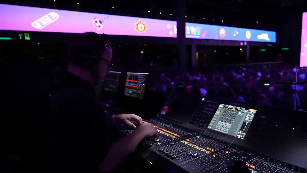 Mãos de técnico operando faders de console durante evento ao vivo
